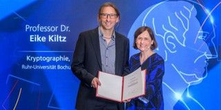 A man and a woman standing in front of a blue background. The man is holding a certificate.