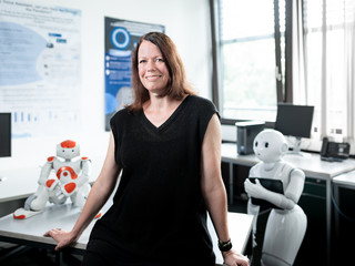 Portrait von Prof. Dr. Nicole Krämer, im Hintergrund stehen zwei Roboter