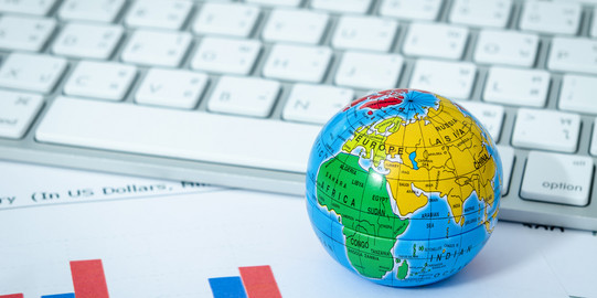 A small colorful globe lies in front of a modern keyboard and on a printout with bar charts