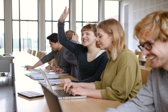 Hörsaal mit Studierenden, von denen sich eine Studentin meldet.