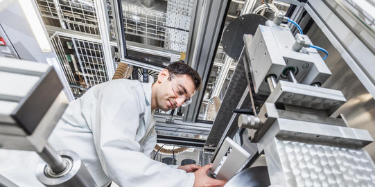 Ein Mann in einem Laboranzug bringt in einem Industrielabor eine Leiste an einer Maschine an