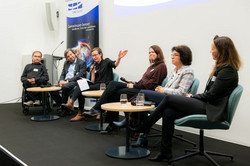 Foto: Eine Gruppe von Personen sitzt auf Stühlen auf einer Bühne. Sie unterhalten sich bei einer Panel-Diskussion.