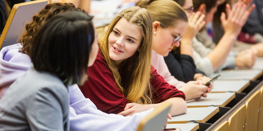 Junge Studierende, vornehmlich Frauen, unterhalten sich in einem Hörsaal an der Universität Duisburg-Essen.