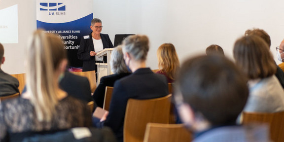 Universitätsallianz vernetzt gefährdete Forschende Isolde Karle steht vor sitzendem Publikum und hält eine Rede.
