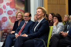 Foto des Publikums bei einem Vortrag. Männer und Frauen in Anzügen sitzen auf Stuhlreihen und lachen.