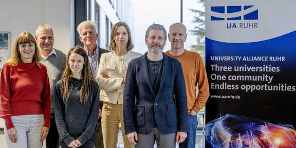 Photo: A group photo of the UA Ruhr Council for Ethics and Responsibility next to a UA Ruhr display. The poster reads: “University Alliance Ruhr. Three universities, one community, endless opportunities”