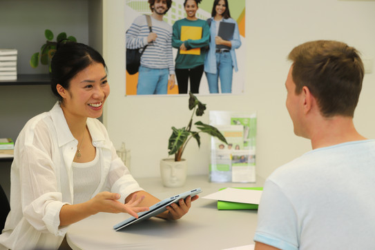 Conversation between a woman, iPad in hand, and a man at a table at the student counselling service.
