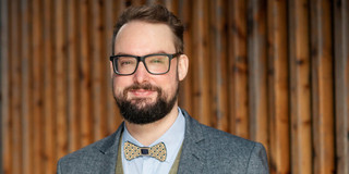 Portrait photo of Prof. Dr. Alexander Probst: It shows a man with glasses and a beard wearing a suit with a bow tie.