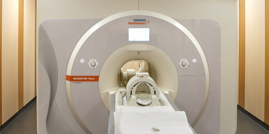 Frontale Sicht auf das MAGNETOM-Terra-7-Tesla-MRT-System im Erwin L. Hahn Institut für Magnetresonanztomographie. Die Liege des MRT ist ausgefahren vor dem Scanner.